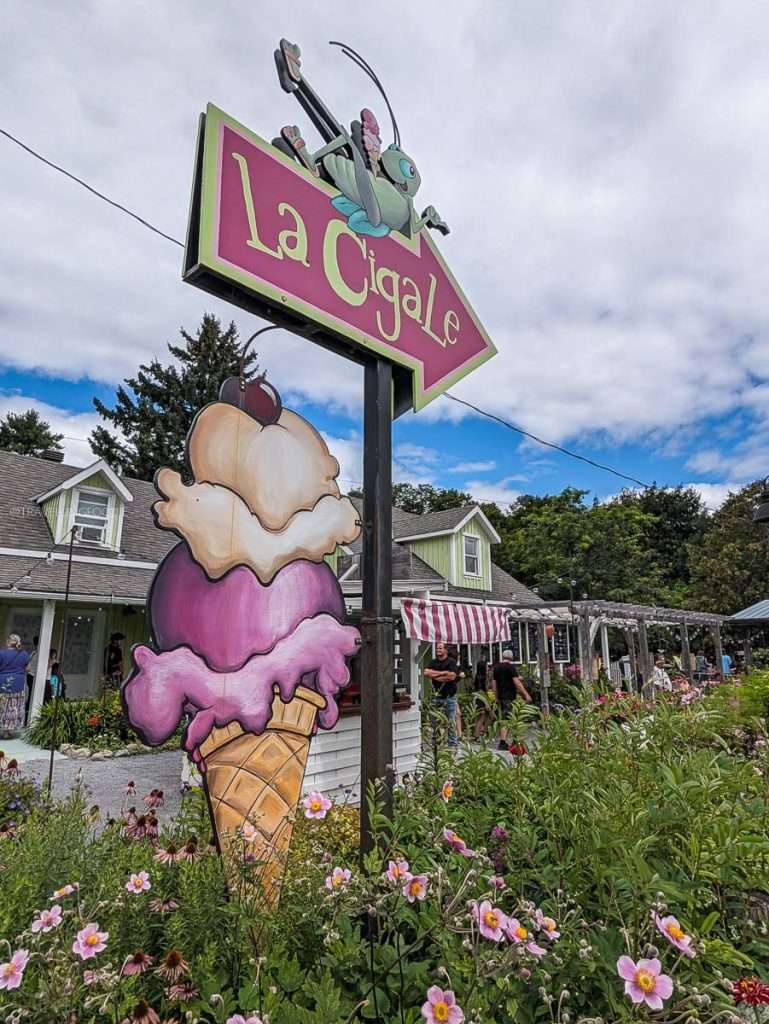 The colorful La Cigale ice cream cone sign surrounded by pink garden flowers, a must-visit dessert spot in Chelsea Quebec.