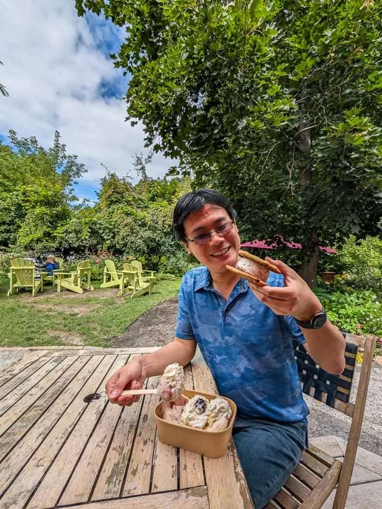 Travelling Foodie Raymond Cua holding an ice cream sandwich while enjoying a banana split outdoors at La Cigale in Chelsea Quebec.