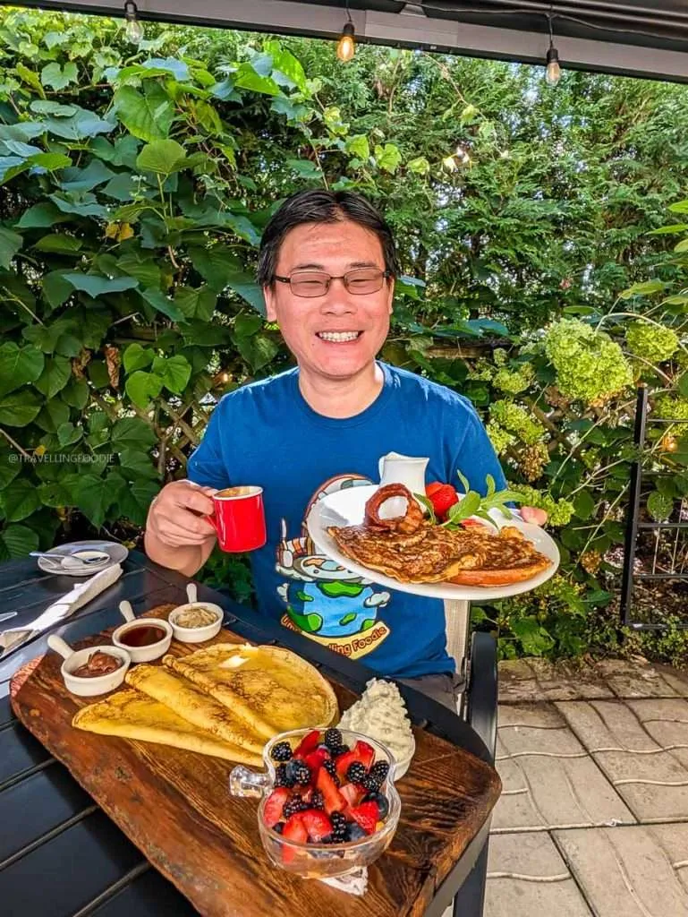 Raymond Cua holding a coffee and French toast with a massive crepes platter at Le Cafe Entre Amis in Montebello Quebec.