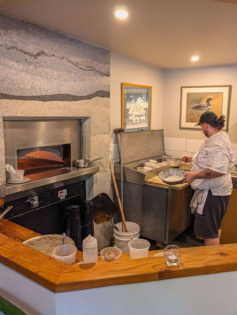 A chef preparing food next to the pizza oven inside Les Fougeres, an award-winning fine dining restaurant in Chelsea.