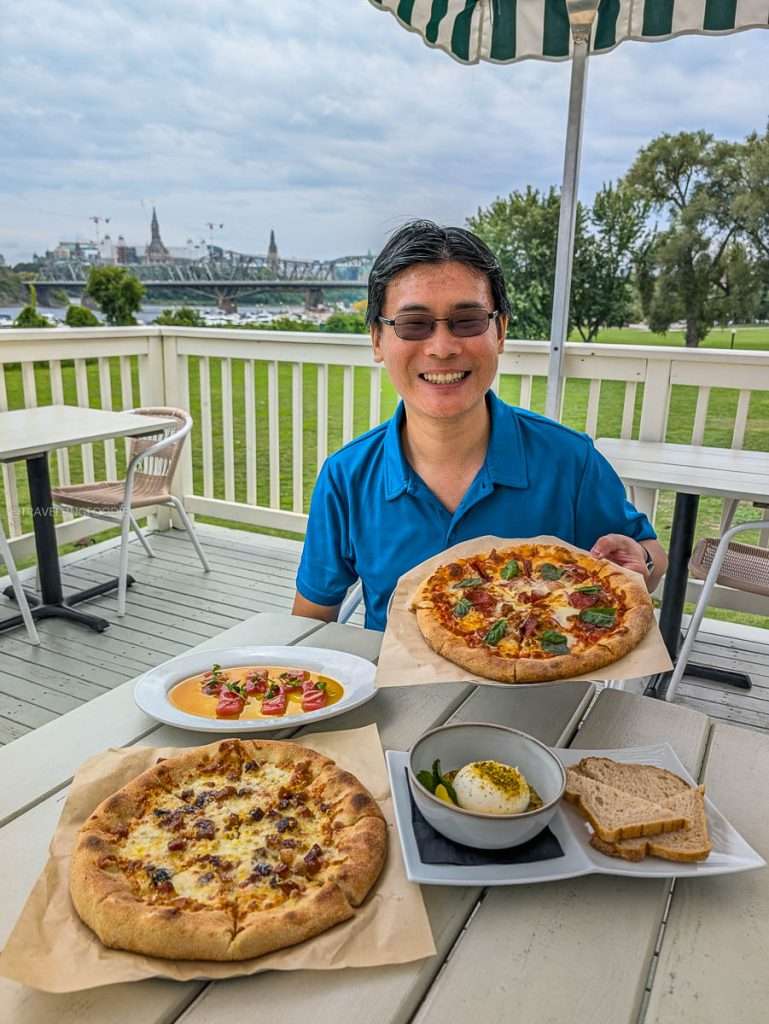 Raymond Cua holding wood-fired pizza on the riverside patio at Maison Charron, a top Gatineau Quebec restaurant.