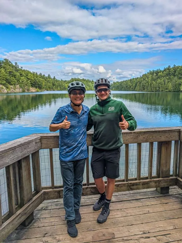 Raymond Cua and guide Vincent giving thumbs up at Pink Lake in Gatineau Park during an e-bike tour
