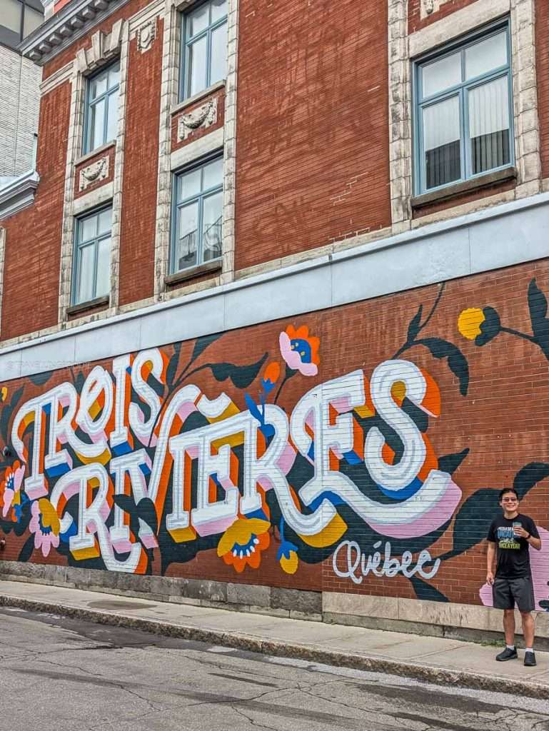 Travelling Foodie Raymond Cua standing next to a colorful Trois-Rivieres mural on a brick building during my Lanaudiere-Mauricie trip
